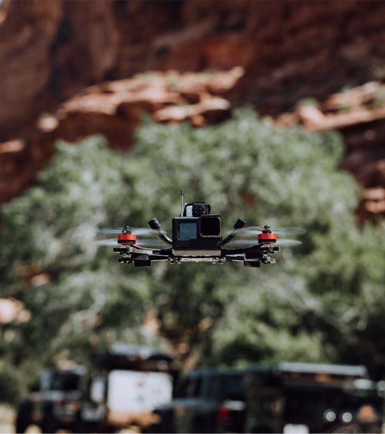 Focus on drone flying in front of a vehicle in front of a giant bush in the valley of a desert